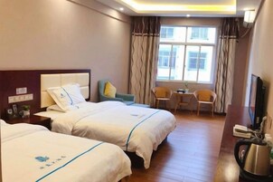 A hotel room with two beds, a desk, a chair, a window with curtains, and a television.