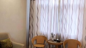 A room with a sofa, two wicker chairs, a small round table, and a curtain with a wavy pattern. - Huating Hotel (Mojiang)