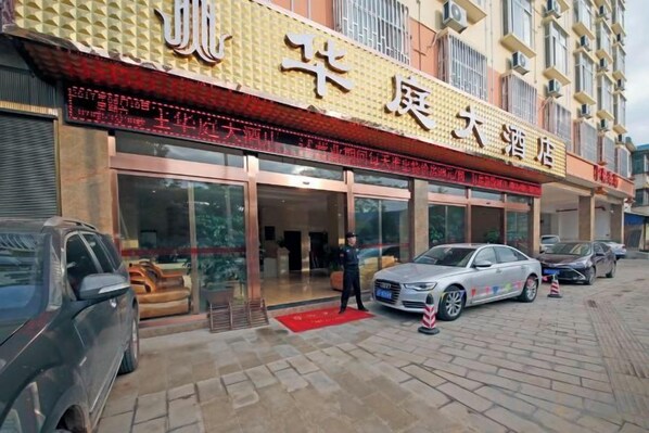 A hotel with a red awning and multiple entry points. There are cars parked in front and a person standing near the entrance.