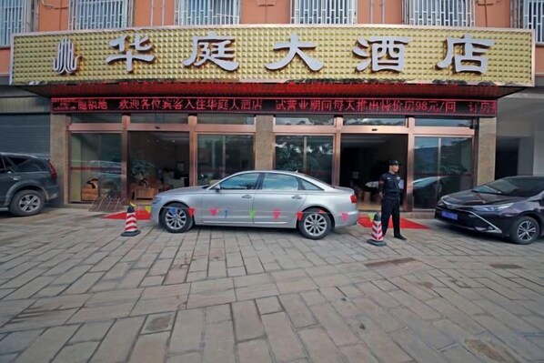 A hotel entrance with a car parked in front and a person standing by the entrance. - Huating Hotel (Mojiang)