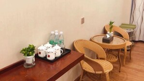 A room with a wooden table set with teapots, cups, and bottles, wicker chairs, and a small potted plant. - Huating Hotel (Mojiang)