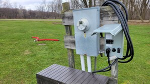 An outdoor electrical box with a digital display, connected to a wooden post and a metal box. - Pondside Campground (Meadville)