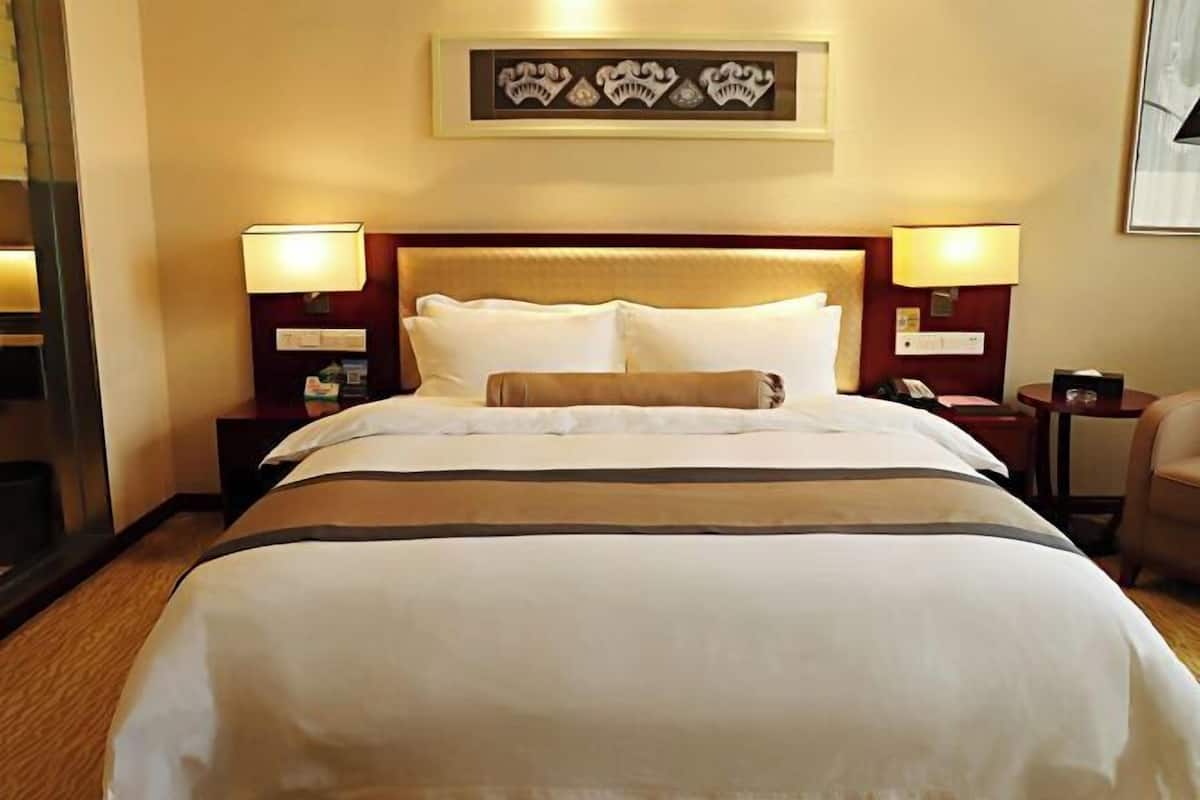 Quarto de hotel com uma cama grande, duas mesas de cabeceira com luminárias, uma obra de arte emoldurada acima da cama e uma cadeira no canto.