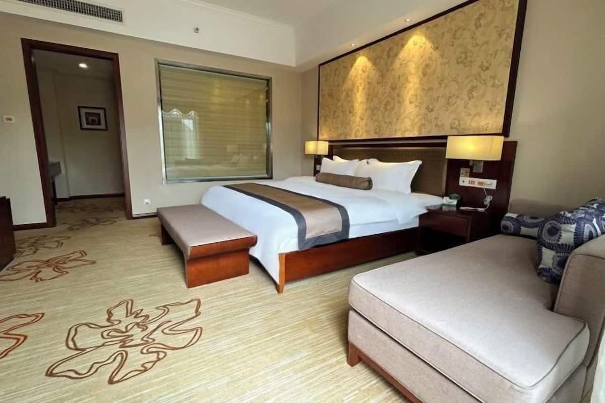 Quarto de hotel com uma cama grande, uma mesa de cabeceira, uma luminária, um banco e um sofá.
