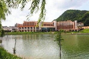 Un hotel con un edificio grande, un lago al frente y un paisaje montañoso de fondo.