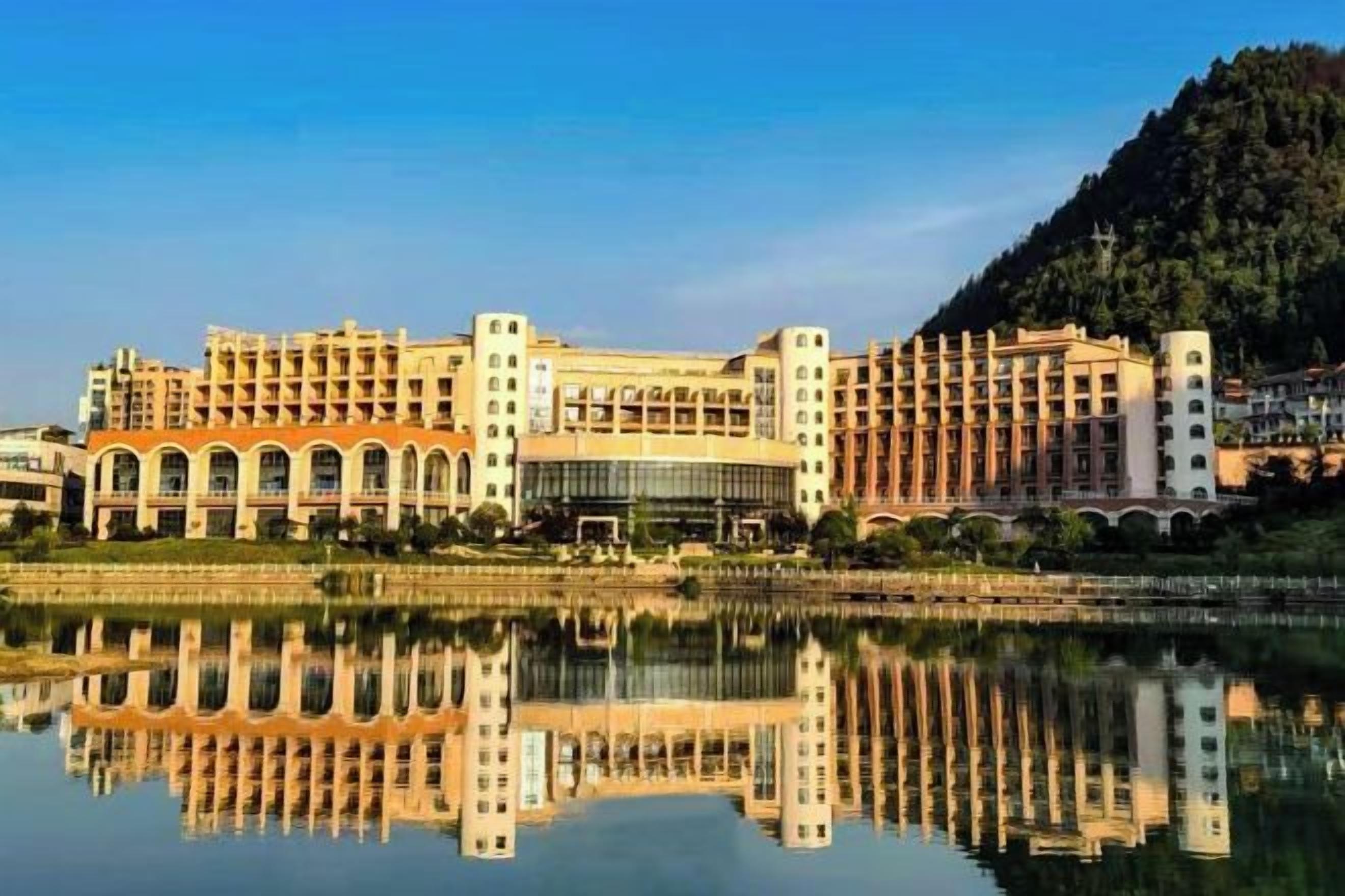 A large hotel with multiple floors, a central courtyard, and a reflection in the water.