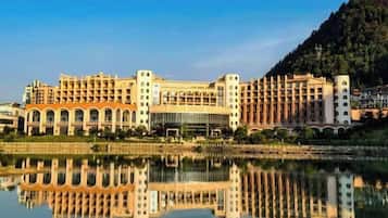 A large hotel with multiple floors, a central courtyard, and a reflection in the water.