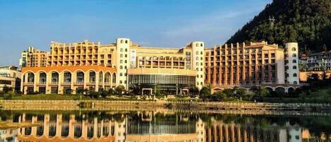 A large hotel with multiple floors, a central courtyard, and a reflection in the water.