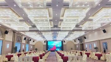 A banquet hall with rows of tables, a stage at the front, and chandeliers.