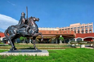 A statue of a mounted figure in front of a hotel with a modern architectural style, large windows, and a well-maintained garden.