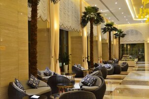 Un hall de hotel con zonas de estar, palmeras y un mostrador de recepción.