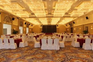 Une salle de banquet avec des rangées de tables et de chaises, une scène et un sol recouvert de moquette.