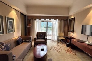 A modern hotel room with a sofa, armchair, round coffee table, and a TV.