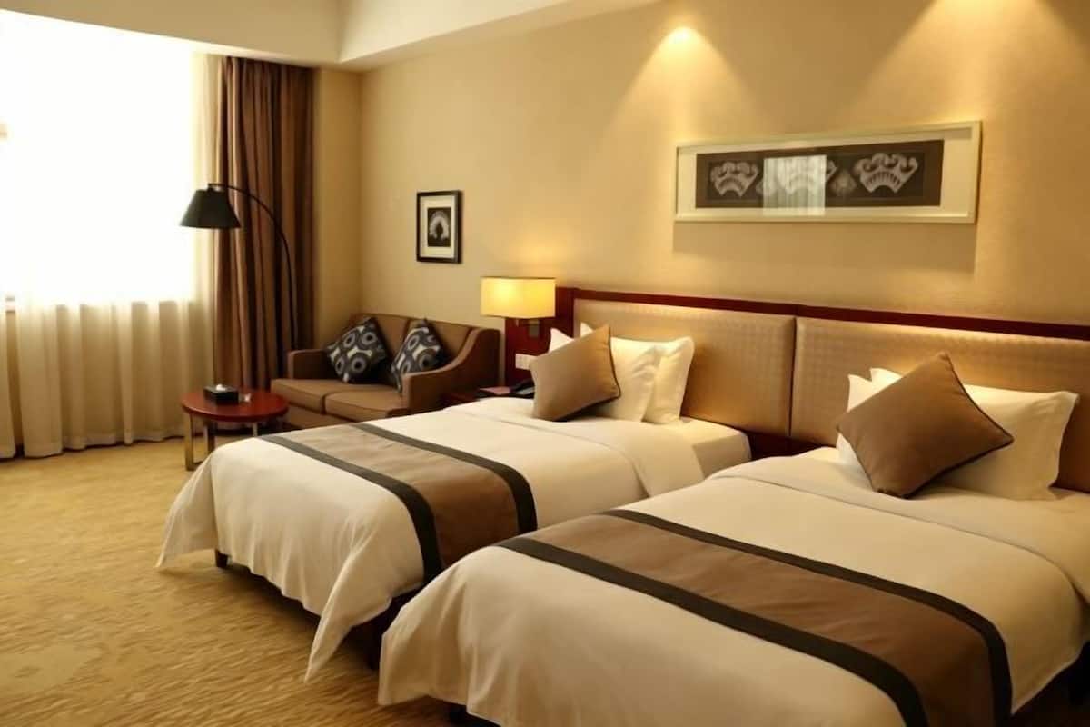 Quarto de hotel com duas camas, um sofá, uma luminária e um quadro na parede.