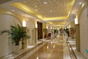 Un couloir d’hôtel avec un sol ciré, un plafond décoratif et des plantes en pot.
