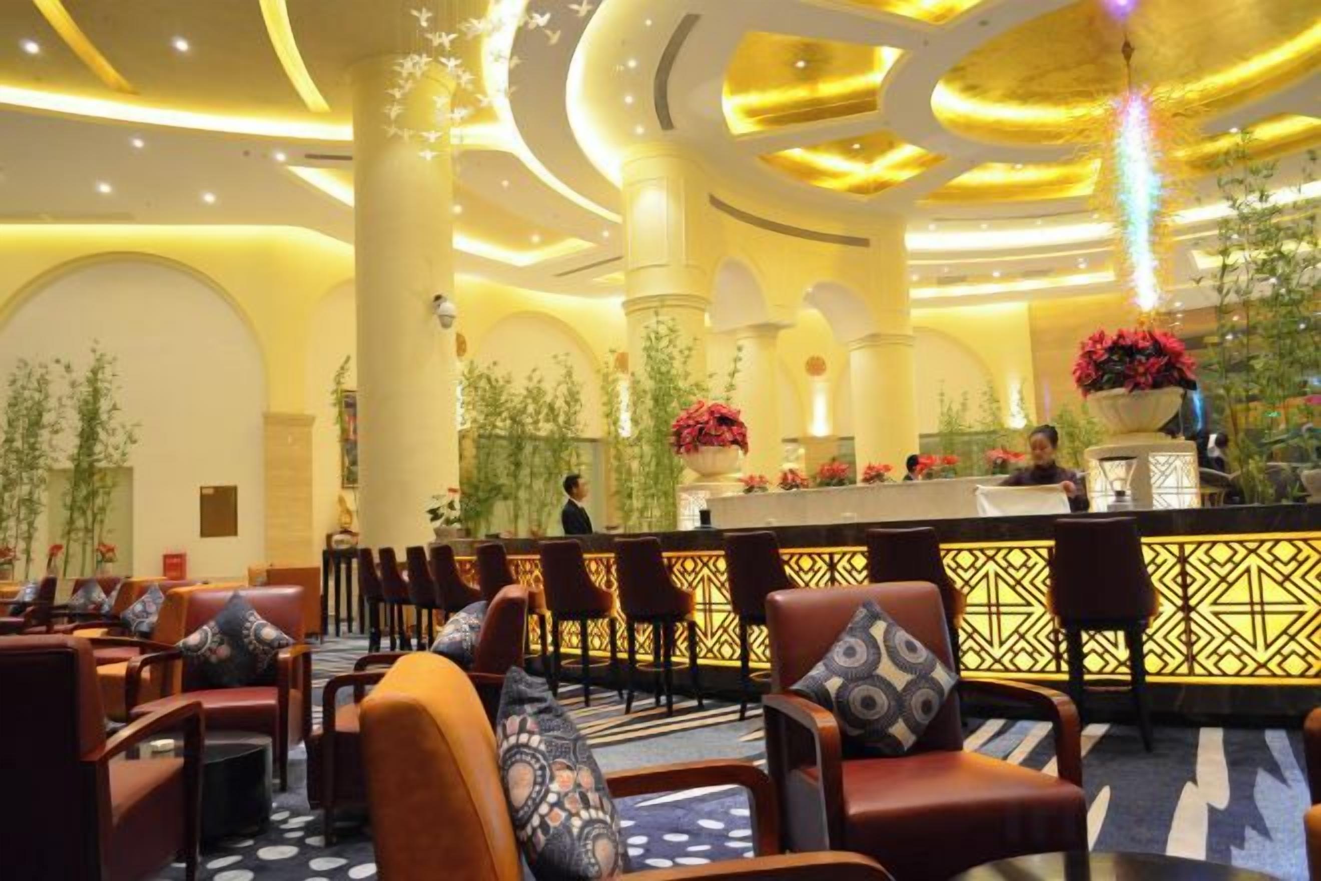 Un hall de hotel con mostrador de recepción, zona de estar y plantas decorativas.