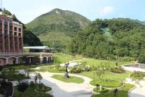 A hotel courtyard with a central sculpture, surrounded by greenery and a mountain backdrop. - Island International Hotel (Liupanshui)
