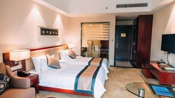 A hotel room with two beds, a desk, a chair, a TV, and a glass table.