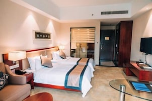 A hotel room with two beds, a desk, a chair, a TV, and a glass table.