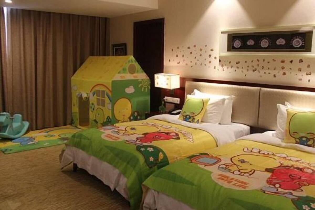 Quarto de hotel com duas camas, um espaço de brincadeira infantil e uma parede decorada com pequenas imagens.