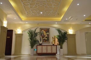 Vestíbulo de hotel con un techo decorativo, una recepción y plantas en macetas.