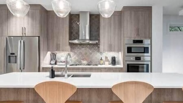 Une cuisine moderne dotée d’un îlot central, d’appareils électroménagers en acier inoxydable et de meubles de rangement en bois.