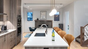 Une cuisine moderne dotée d’un îlot central, de fours encastrés et d’un luminaire suspendu.