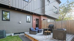 Une terrasse extérieure moderne, équipée d’un barbecue, d’un espace salon et de guirlandes lumineuses.