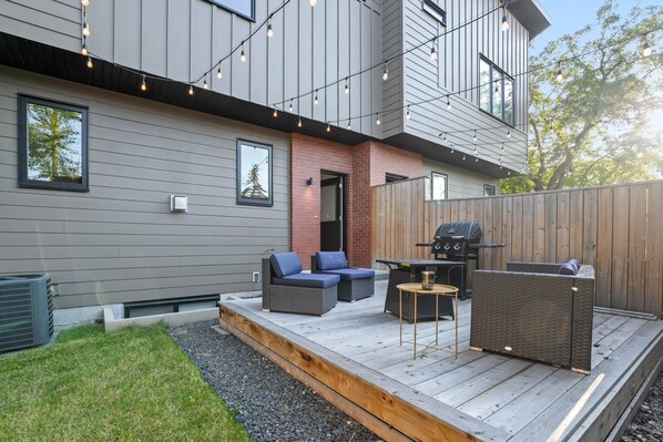 A modern outdoor patio with a grill, seating area, and string lights. - Empire: Upscale 4 Bedroom in Trendy Marda Loop - Garage, A/C (Calgary)