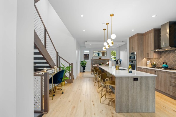 A modern kitchen with a central island, wooden cabinets, and pendant lighting. - Empire: Upscale 4 Bedroom in Trendy Marda Loop - Garage, A/C (Calgary)