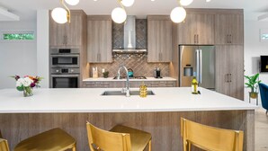 Une cuisine moderne dotée d’un îlot central, d’appareils électroménagers en acier inoxydable et de luminaires suspendus.