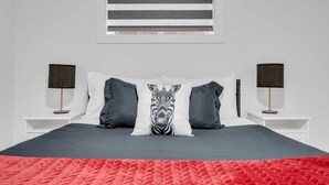 Ein Bett mit einem Zebra-Kissen, zwei Nachttischlampen und einem Fenster mit horizontalen Jalousien.