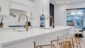 Uma cozinha moderna com armários brancos, torneiras douradas e uma ilha grande com banquetas.