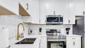 A modern kitchen with white cabinetry, a stainless steel microwave, and a built-in oven. - The Olaf in Trendy Killarney - Close to Everything (Calgary)