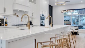 Une cuisine moderne avec des meubles blancs, des accessoires dorés et un grand îlot central doté de tabourets de bar.