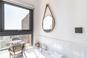A modern bathroom with a large window, a round mirror, a white sink, and a chair by the window. - Qingdao Qigu Abalone Island No.85 Homestay (Qingdao)