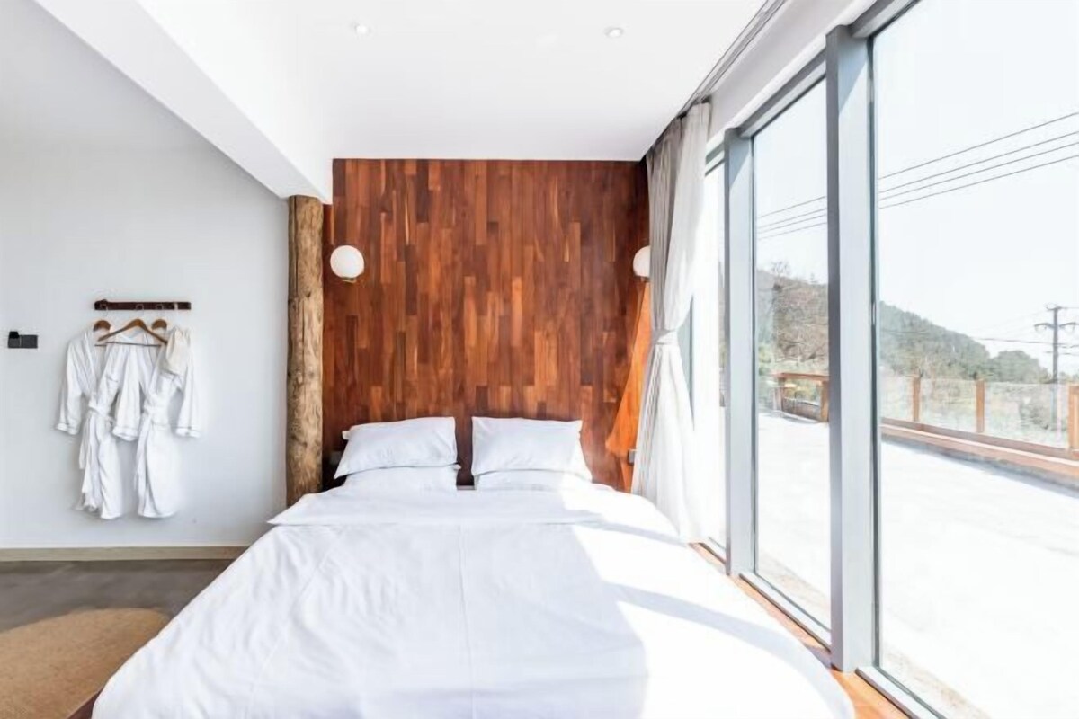 Quarto moderno com parede em madeira, uma cama grande e vista para o exterior.