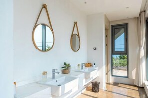 A bathroom with three sinks, two mirrors, and a window.