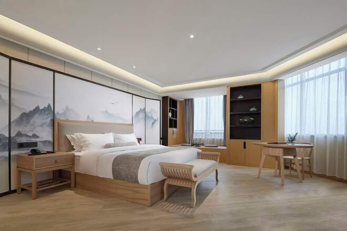Een moderne slaapkamer met een groot bed, nachtkastjes, een houten bankje, een bureau en een boekenkast.