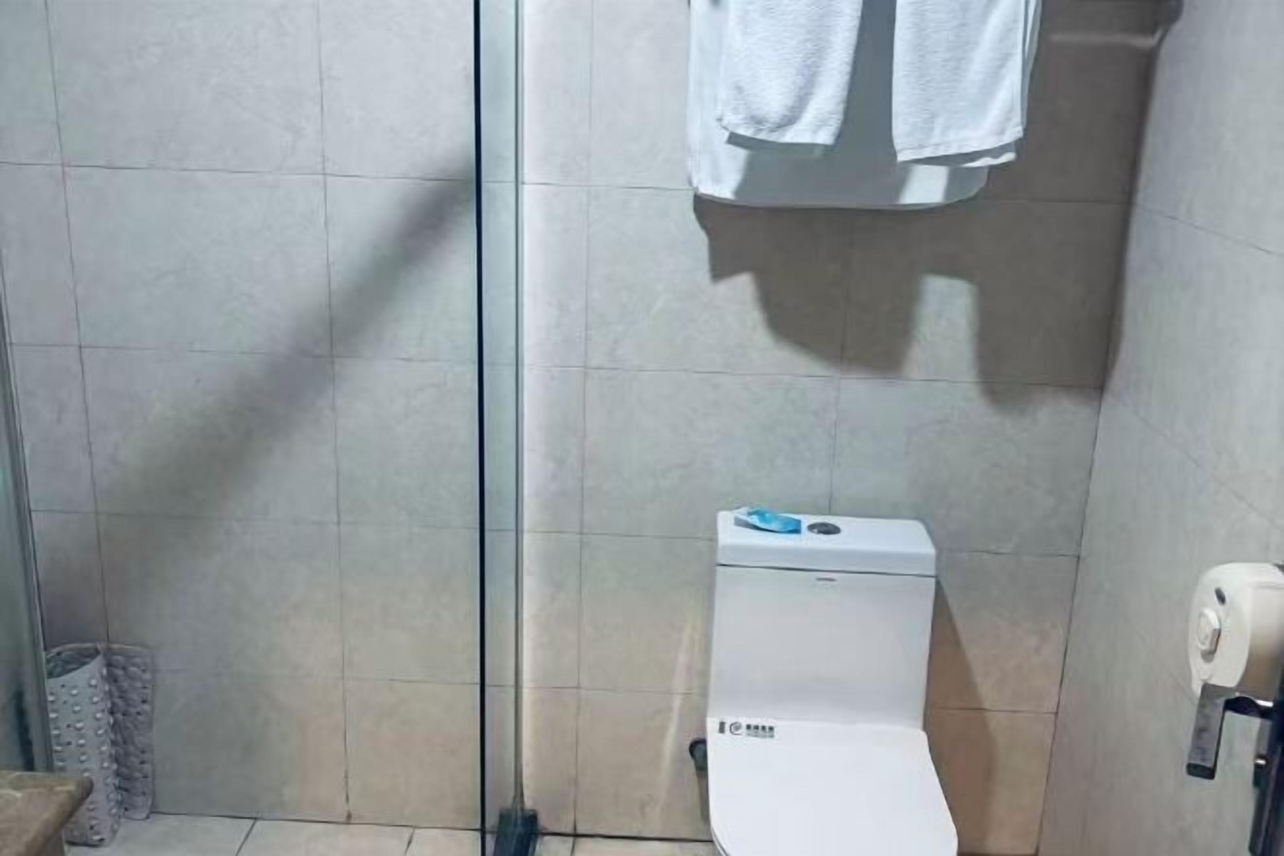 Een badkamer met een toilet, een handdoekrek met een handdoek en een douchegedeelte.