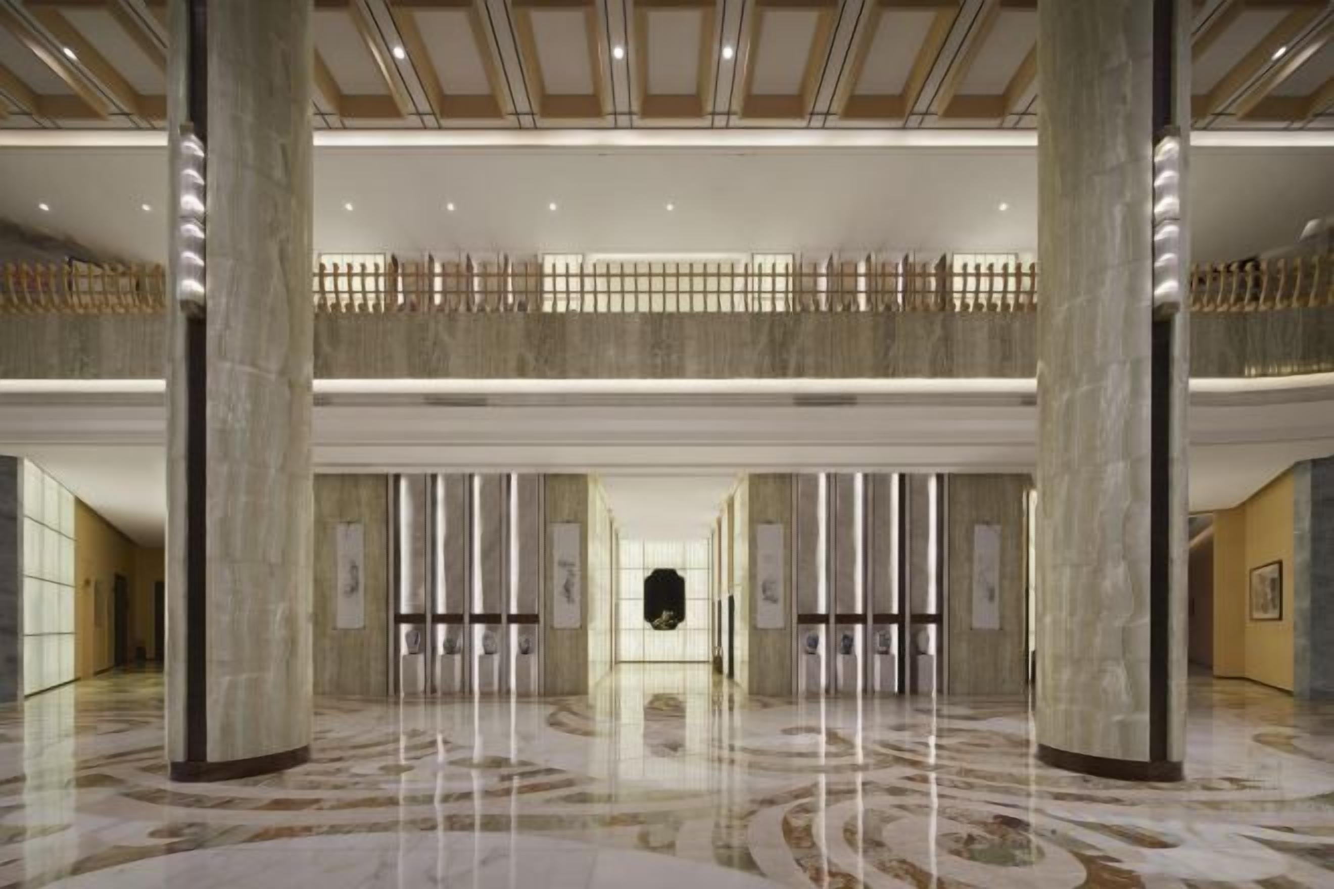 A spacious lobby with marble flooring, high ceilings, and a central column.