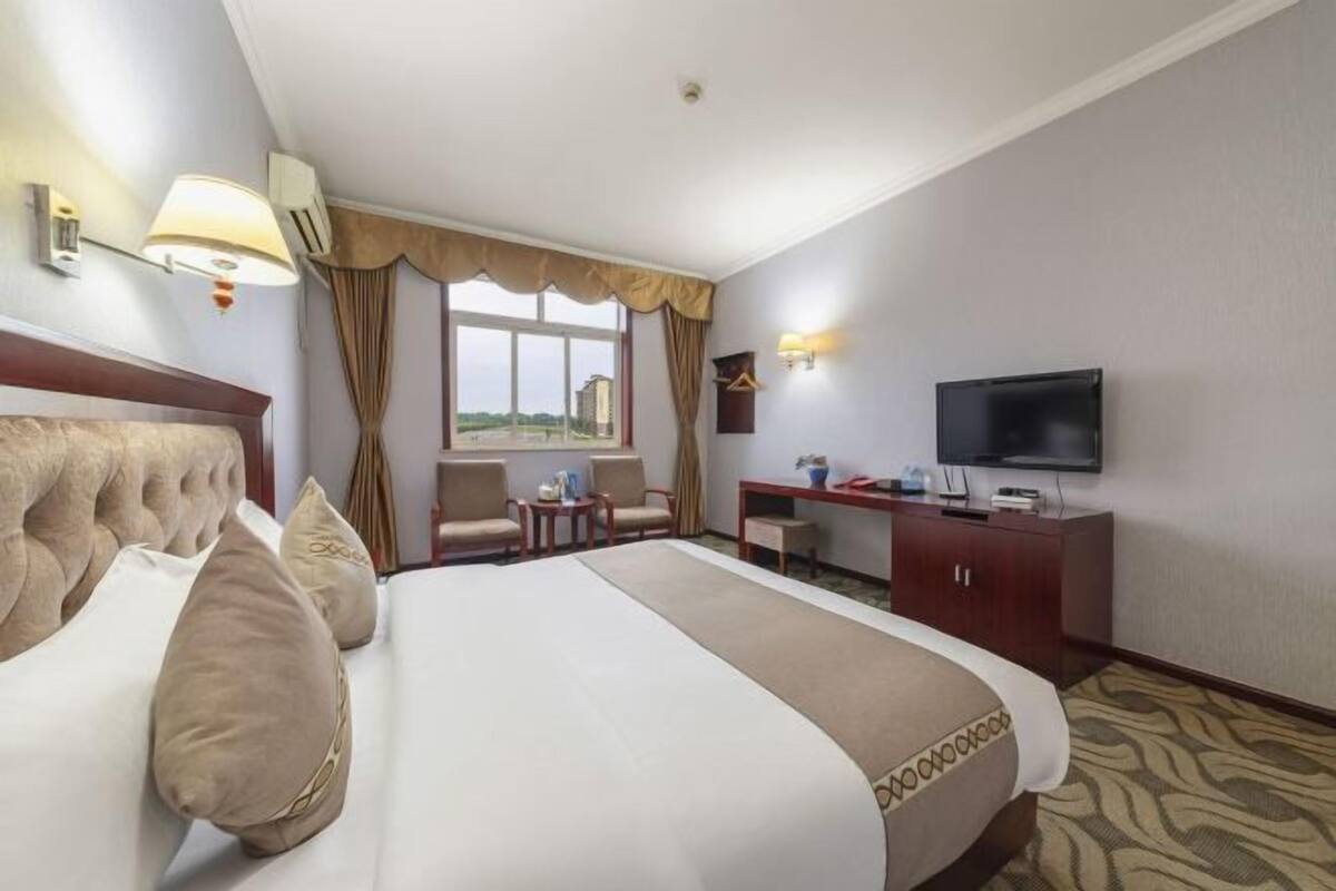 Een hotelkamer met een groot bed, een bureau, een televisie en een raam met gordijnen.