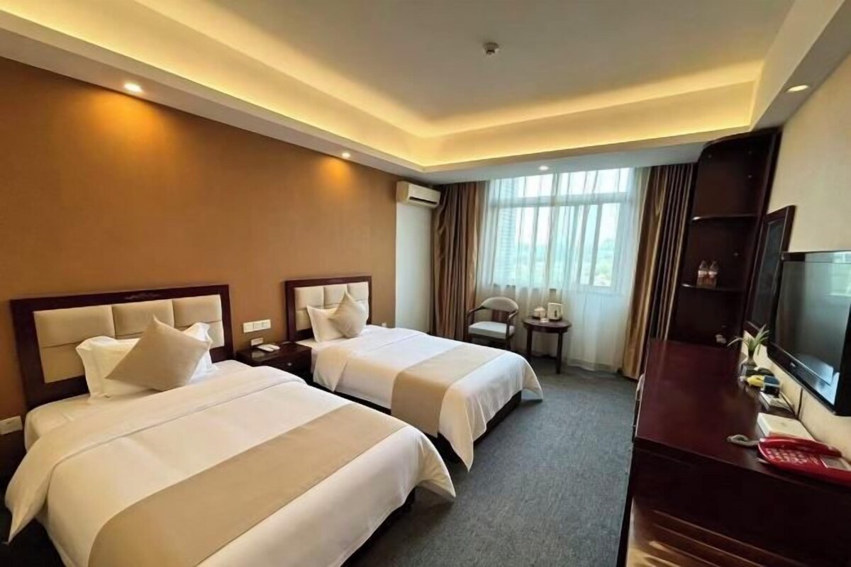 Een hotelkamer met twee bedden, een bureau, een televisie en een raam met gordijnen.