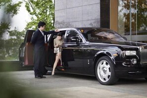 Une voiture de luxe noire, dont un homme et une femme sortent.