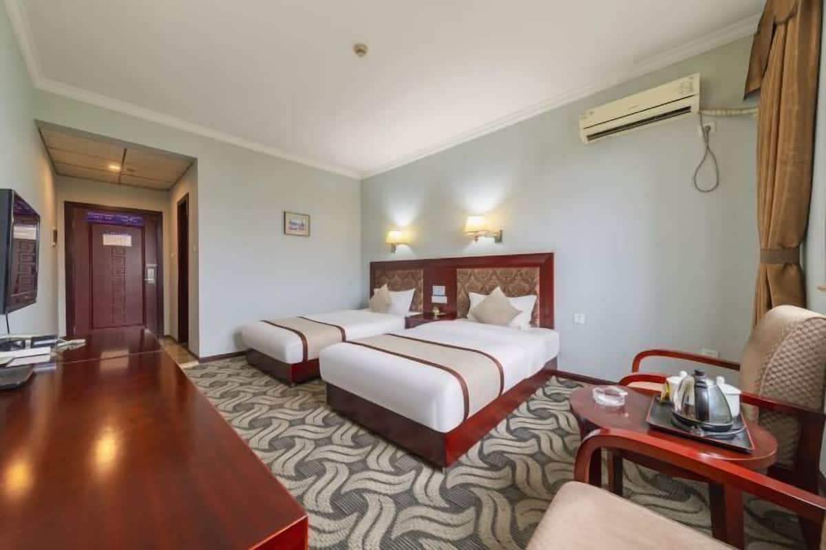 Een hotelkamer met twee bedden, een houten bureau, een stoel, een klein tafeltje met dienblad en een airconditioning.