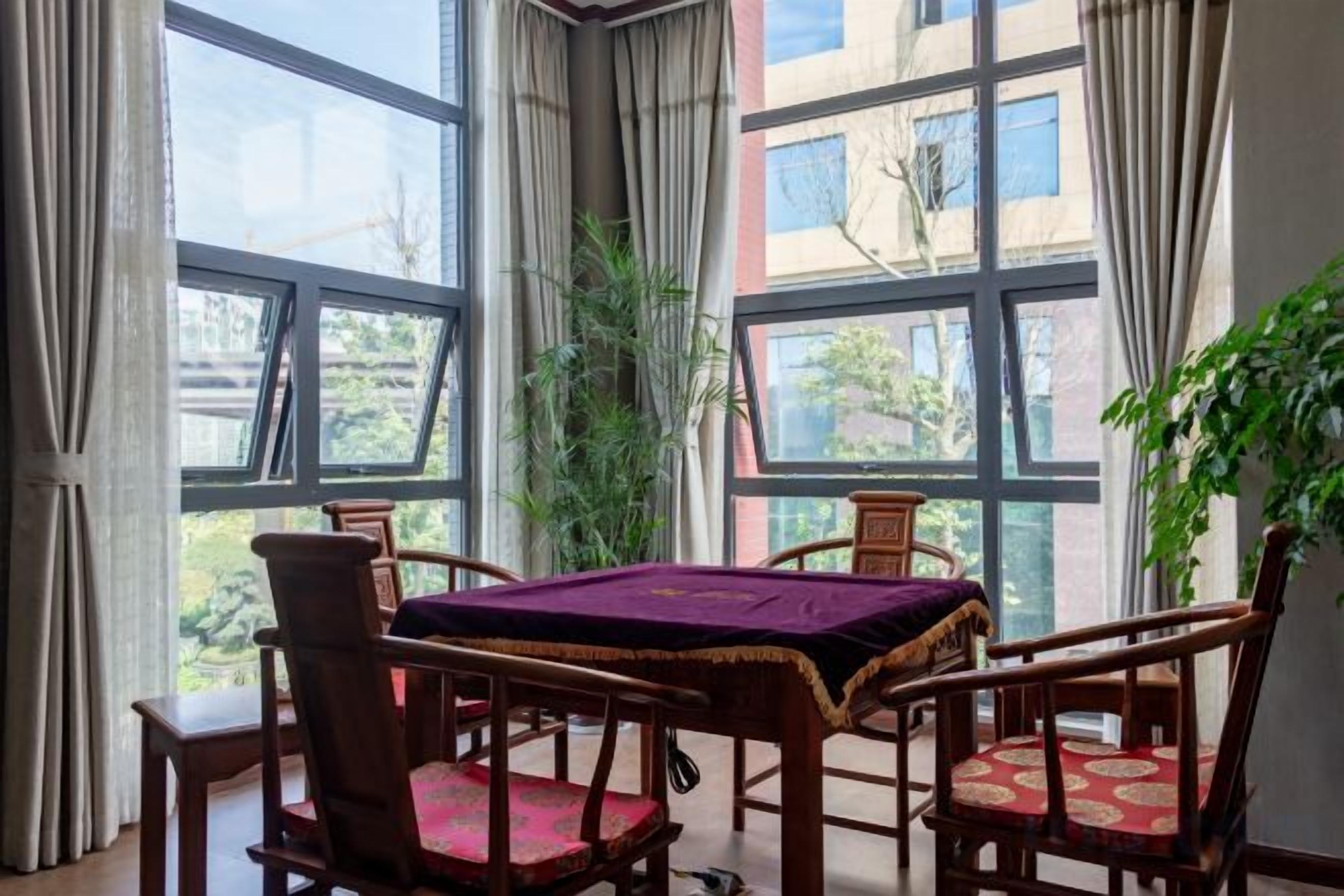 Una habitación con una mesa y sillas, ventanas amplias y vistas a edificios.