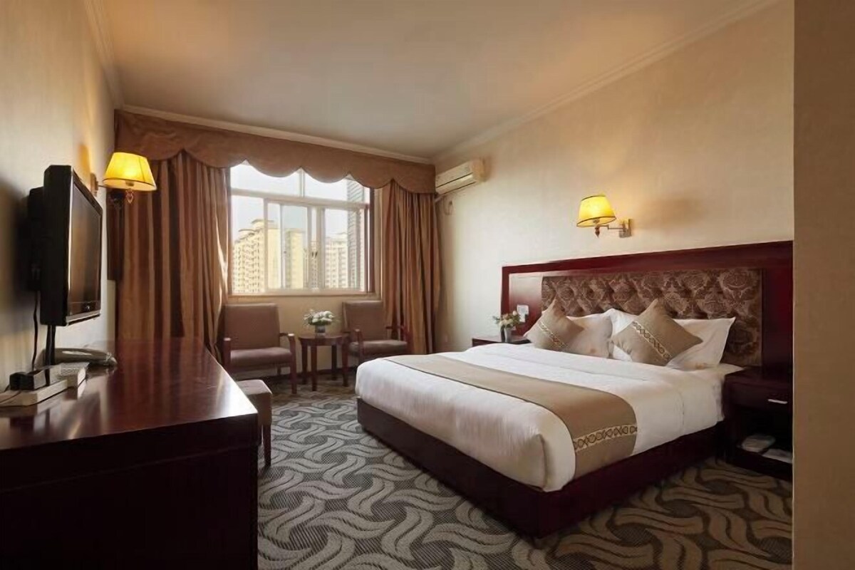 Habitación de hotel con una cama grande, un escritorio, un televisor y una ventana con cortinas.