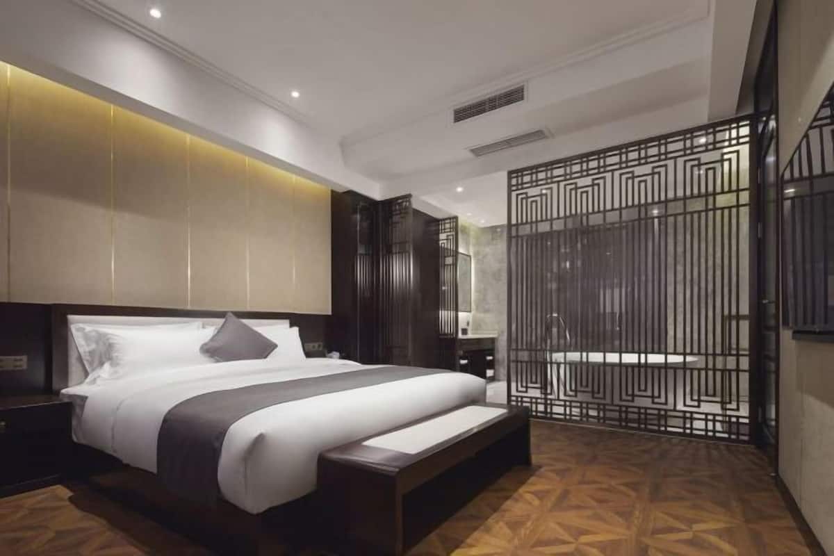 Een moderne hotelkamer met een groot bed, een bankje, een houten vloer en een decoratieve scheidingswand.