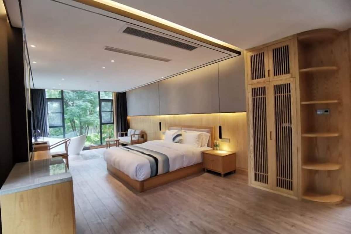 Een moderne slaapkamer met een groot bed, nachtkastjes, een houten garderobe en uitzicht op groen.
