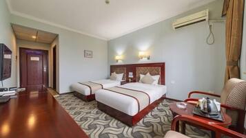 A hotel room with two beds, a desk, a chair, and an air conditioning unit.